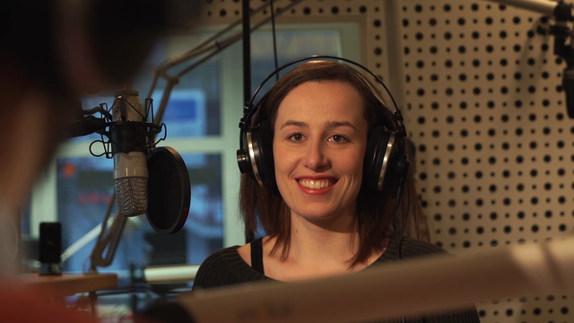 Eine junge Frau im Radiostudio mit Kopfhörer lacht in Richtung Kamera